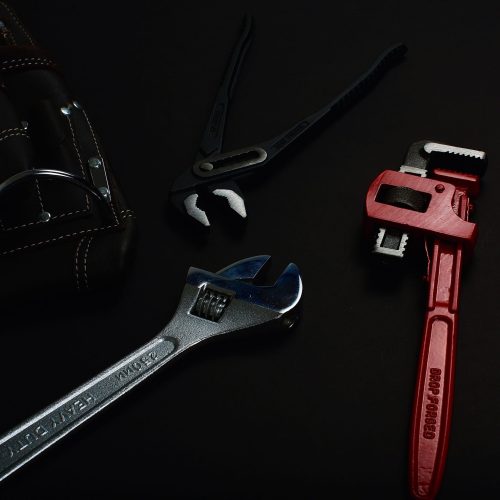 Close-up of various hand tools including wrenches and pliers on a dark surface.