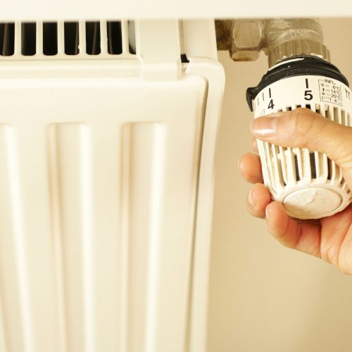 Close-up of hand adjusting radiator thermostat to control home heating temperature.