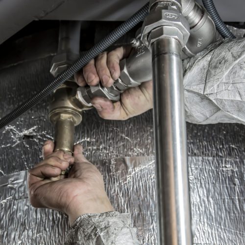 Close-up of a plumber's hands installing steel pipes indoors, showcasing skilled manual work.